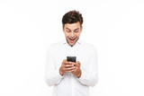 Fototapeta Na ścianę - Happy young man with short dark hair chatting or typing text message with smartphone, isolated over white background