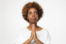African American Woman Isolated On Gray Background, Standing With Palm Pressed To Each Other In Gesture Of Praying, Looking Above As If Waiting For Answer To Question From High Forces