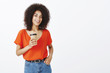 © Cookie Studio - Girl can deal with any task. Confident good-looking african-american female student with afro haircut, holding cup of coffee and hand in pocket, smiling friendly, being self-assured over gray wall