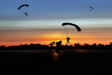 Fototapeta  - Spadochroniarze lądują na płycie lotniska aeroklubu po zachodzie słońca.