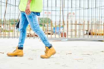 low section portrait of unrecognizable worker wearing jeans and boots crossing construction site, co