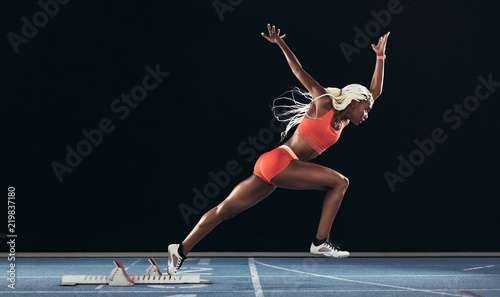 Fotomural Woman athlete taking off from starting block on a running track