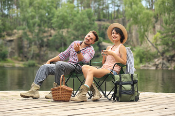 Canvas Print - Young couple resting on pier near lake. Camping season