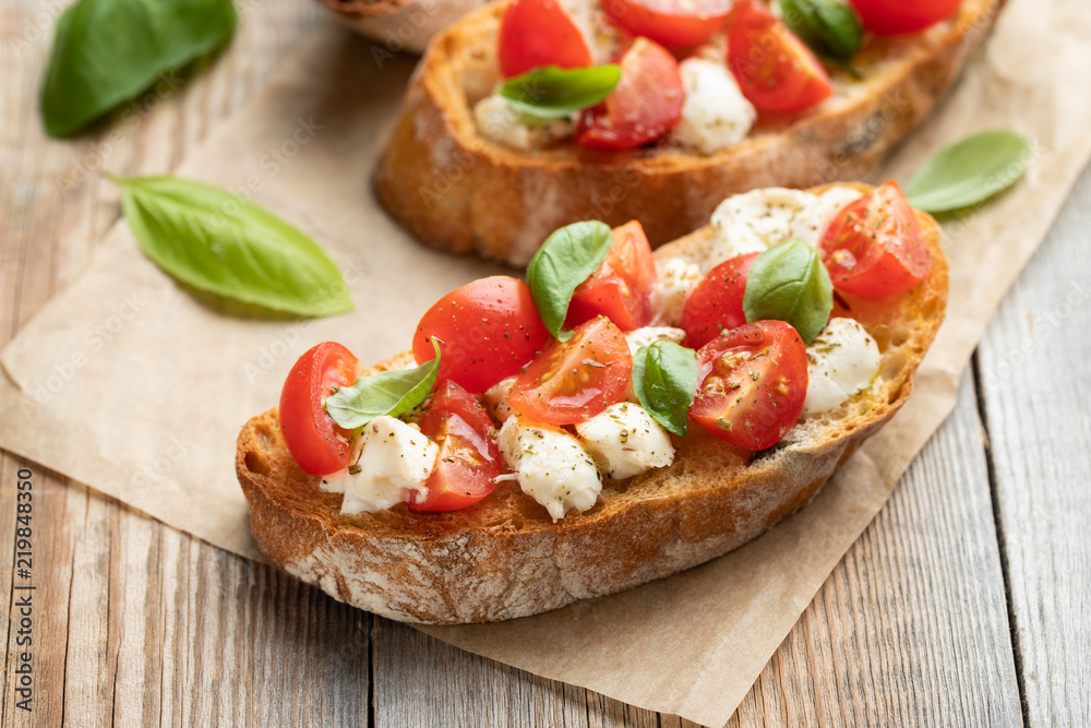 Bruschetta with tomatoes, mozzarella cheese and basil on a old rustic table. Traditional italian appetizer or snack, antipasto - obrazy, fototapety, plakaty 