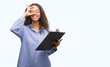 © Krakenimages.com - Young hispanic business woman holding clipboard with happy face smiling doing ok sign with hand on eye looking through fingers