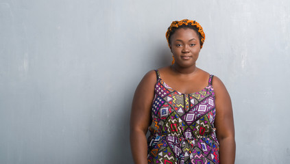 Poster - Young african american woman over grey grunge wall wearing orange braids with serious expression on face. Simple and natural looking at the camera.