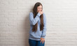 © Krakenimages.com - Young Chinise woman over white brick wall smelling something stinky and disgusting, intolerable smell, holding breath with fingers on nose. Bad smells concept.