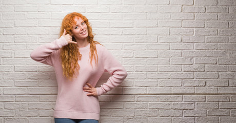 Poster - Young redhead woman standing over brick wall smiling doing phone gesture with hand and fingers like talking on the telephone. Communicating concepts.