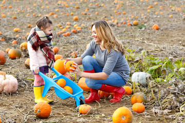 little kid girl and beautiful mother having fun with farming on a pumpkin patch. traditional family 
