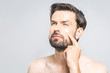 © denis_vermenko - Skin care. Handsome happy young shirtless man applying cream at his face and looking up while standing over gray background and looking at camera. Close-Up. Space for text.