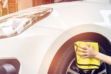 A man cleaning white car with yellow microfiber cloth.