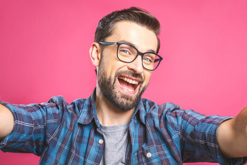 Wall Mural - Portrait of a happy young man taking a selfie photo isolated over pink background. Close-up.