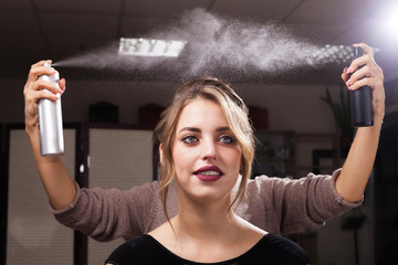 Wall Mural - hairdresser fixing a coiffure of a young beautiful happy client using two hair sprays in a beauty salon. girl having a flawless makeup. concept of professional stylist studying