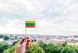 A small Lithuanian paper flag in a woman's hand against a background of a blurred city, the capital of Lithuania Vilnius, welcome to Lithuania