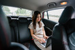© Danon - Portrait of a young Japanese woman getting some work done on her laptop while inside the car. She is being driven to her destination in a ride she booked on a ride hailing app.
