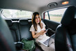 © Danon - Portrait of a young Japanese woman getting some work done while inside the car. She is being driven to her destination in a ride she booked on a ride hailing app.