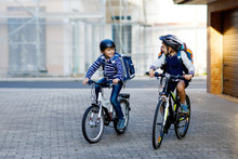 Two School Kid Boys In Safety Helmet Riding With Bike In The City With Backpacks. Happy Children In Colorful Clothes Biking On Bicycles On Way To School. Safe Way For Kids Outdoors To School