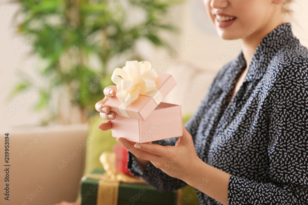 Beautiful young woman opening gift box at home