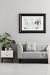 © Photographee.eu - Grey couch with cushion next to white cabinet with plant in flat interior with poster. Real photo
