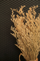 Wall Mural - Brown dried wild flowers bouquet on a black texture background of blurred rhombus texture backdrop.
