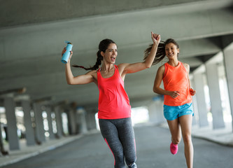 Two female friends jogging and racing through city parking lot.Celebrating win.