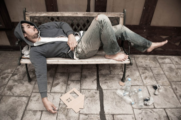 Poor homeless man sleeping on the wooden bench with his cardboard house on the street