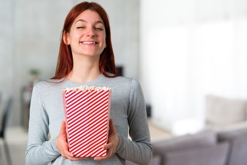 Young redhead girl eating popcorns on unfocused background