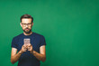 © denis_vermenko - Always in touch. Smiling young man holding smart phone and looking at it. Portrait of a happy man using mobile phone isolated over green background.