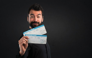 Wall Mural - Handsome man with beard holding air tickets on black background