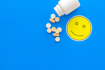 Sticker - Reception of medicines concept. Recovery. Pills falling out of jar near smile face emoji on blue background top view copy space