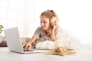 young woman listens to the shell lying in the living room in front of the computer on white wide window in the background