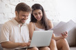 © fizkes - Happy young couple relaxing on couch holding laptop and papers, smiling millennial spouses excited by good news read in mail, husband and wife having fun at home when checking bills and letters