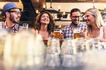 Wall Mural - Young cheerful people in the beer pub drinking and having good time. Friendship concept with young people enjoying time together and having genuine fun at cool vintage pub 