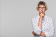 Portrait of pensive thoughtful blonde young woman wears polka dot shirt and glasses feels displeased and looks to the side isolated over white background