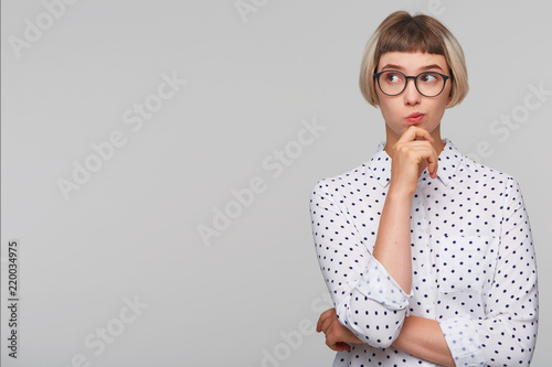 Fotomural Portrait of pensive thoughtful blonde young woman wears polka dot shirt and glas