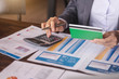 © nopparat - Businesswoman using calculator to calculate saving account passbook and statement with financial report.Female accountant or banker use calculator. Savings, finances and economy concept.
