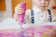 Child paints table with paint on transparent glass, concept development of kid motor skills of hands and art.