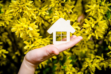 The girl holds the house symbol against the background of blossoming forsythia 