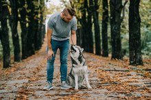 Man With Siberian Husky Dog In Autumn Park