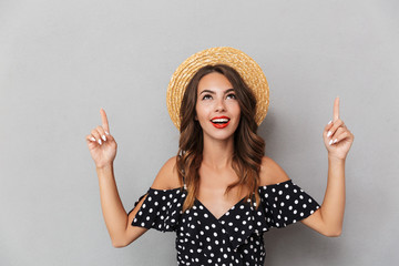 Canvas Print - Cute woman wearing hat pointing over grey wall.