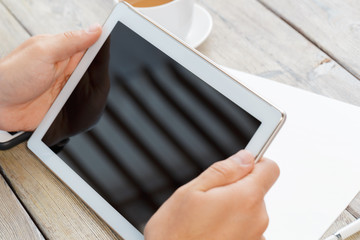 hands of a man holding tablet device over a wooden workspace table