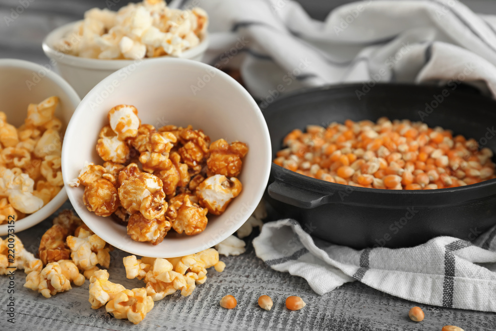 Bowls with delicious popcorn and kernels on wooden background