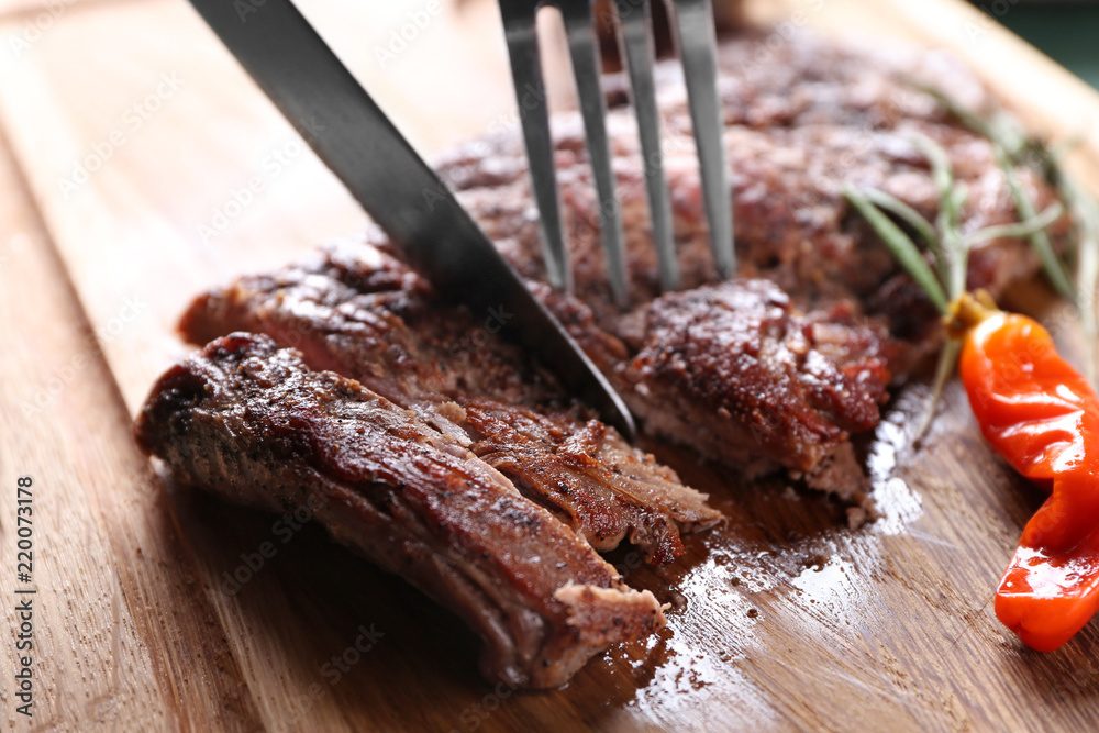 Cutting grilled steak on wooden board, closeup