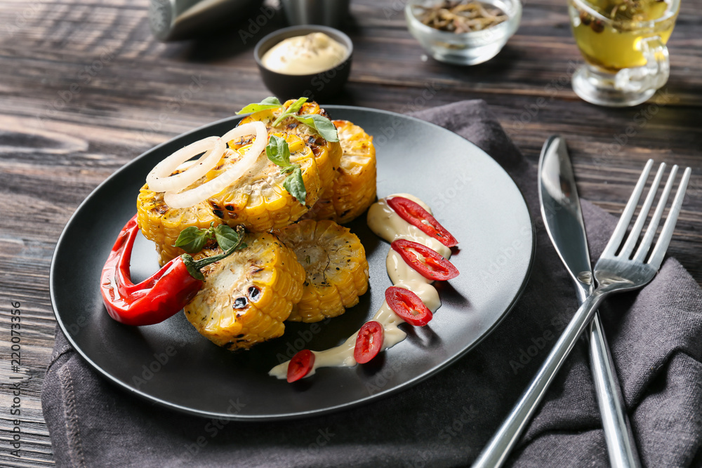 Plate with delicious grilled corn on wooden table