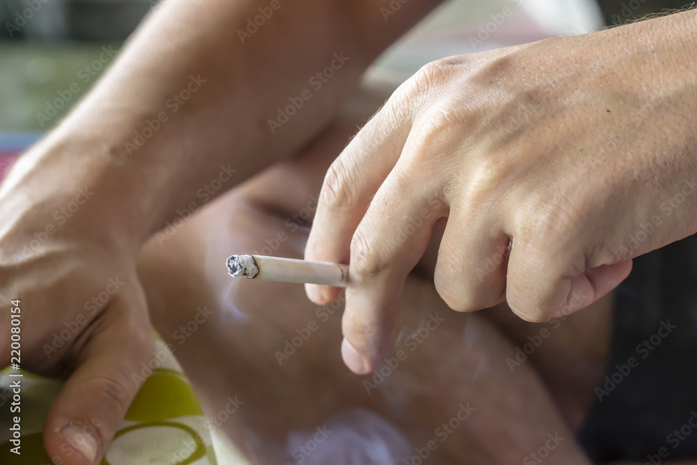 left hand holding cigarette Man smokes cigarette with his left hand under sunlight Stock Photo
