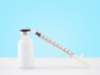 Blank label medical glass vial and plastic syringe for injection on white table with blue gradient background. Concept of vaccination, insulin and cosmetic injection. Copy space.