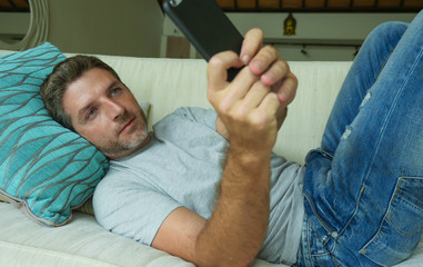 lifestyle indoors portrait of young happy and attractive man at home sofa couch using internet social media app on mobile phone networking relaxed