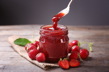 glass jar and spoon with delicious strawberry jam on wooden table