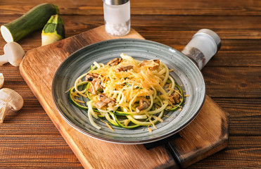 Plate with zucchini spaghetti, mushrooms and cheese on wooden table