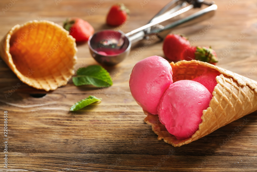 Waffle cone with delicious strawberry ice-cream on wooden background